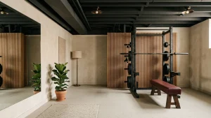 Finished basement gym with joists and ducts painted charcoal, an oak slat screen hiding the mechanicals, a black rack and a full-height mirror