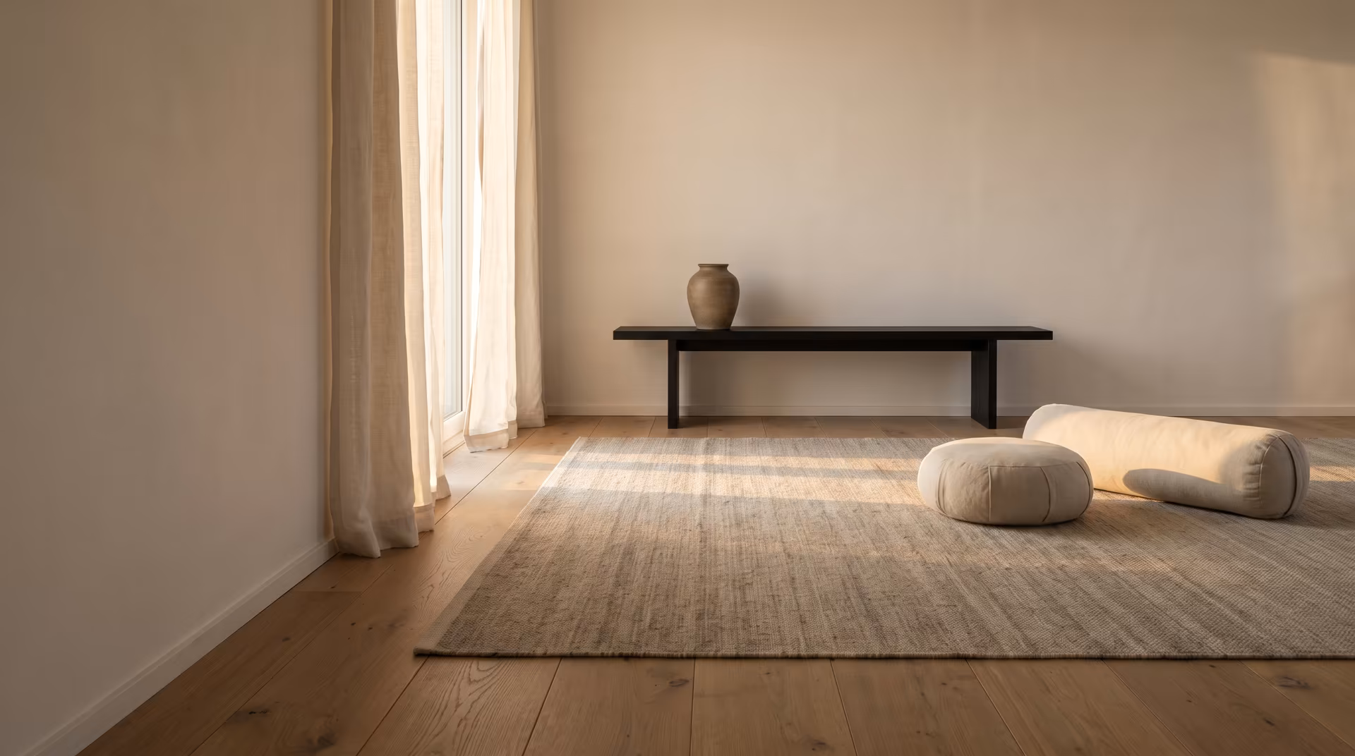 Quiet wellness room with a woven rug, a low black bench, a ceramic vase and a meditation cushion with bolster in daylight