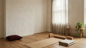 Minimalist home yoga room with a jute mat, cork blocks and folded wool blanket on a wide oak floor beside a linen-curtained window
